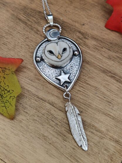 A bezel set porcelain owl face in a handmade silver pendant with moon and star